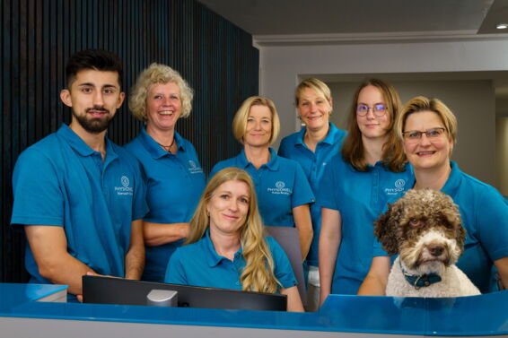Immer für Sie da - Das Praxis-Team der Physiotherapie Neelsen Das Praxis Team steht draußen hintereinander gereiht vor dem Praxisschild.